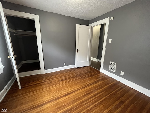 unfurnished bedroom featuring visible vents, baseboards, wood finished floors, a closet, and a textured ceiling