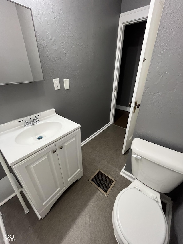 half bath featuring visible vents, baseboards, toilet, a textured wall, and vanity