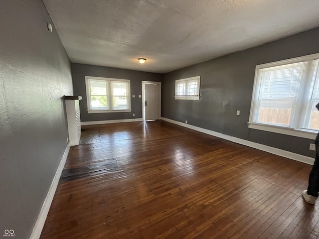 empty room with baseboards, a textured ceiling, a healthy amount of sunlight, and hardwood / wood-style floors