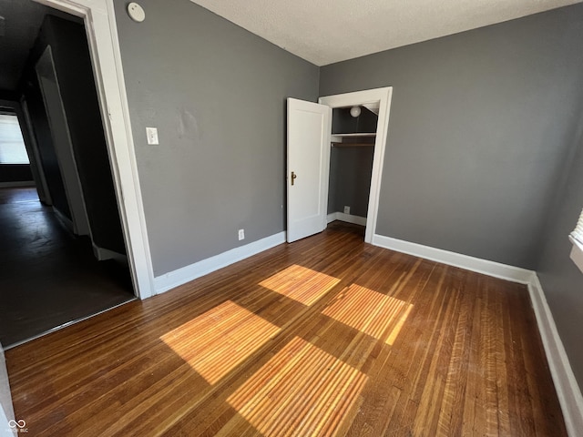 unfurnished bedroom featuring a closet, a textured ceiling, baseboards, and wood finished floors