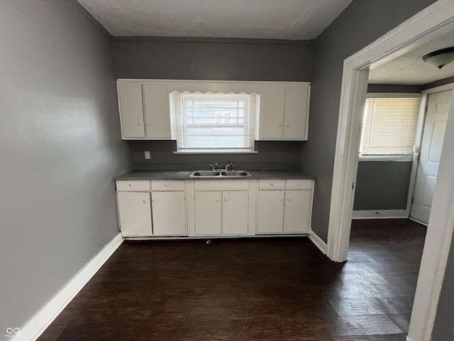 kitchen with a sink, baseboards, and white cabinets