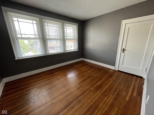 unfurnished room with baseboards, a textured ceiling, and dark wood-style flooring