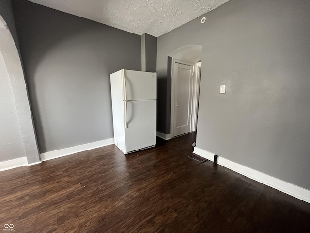 empty room with visible vents, a textured ceiling, arched walkways, baseboards, and dark wood-style flooring