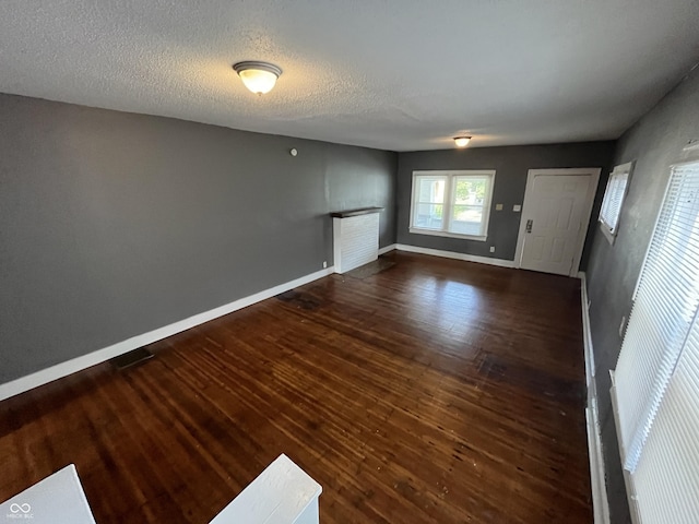 unfurnished living room featuring a textured ceiling, baseboards, and wood finished floors