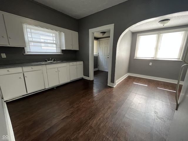 kitchen featuring baseboards, arched walkways, a sink, dark wood-type flooring, and white cabinetry