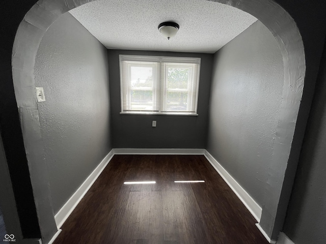 spare room with arched walkways, a textured wall, baseboards, and wood finished floors