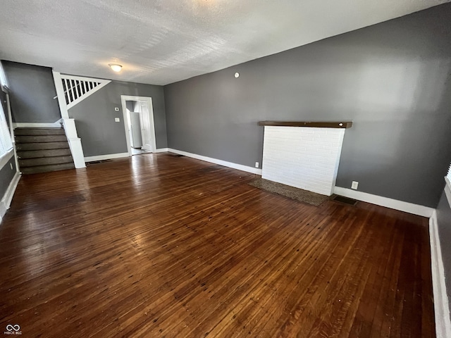 unfurnished living room with stairway, baseboards, a textured ceiling, and hardwood / wood-style flooring