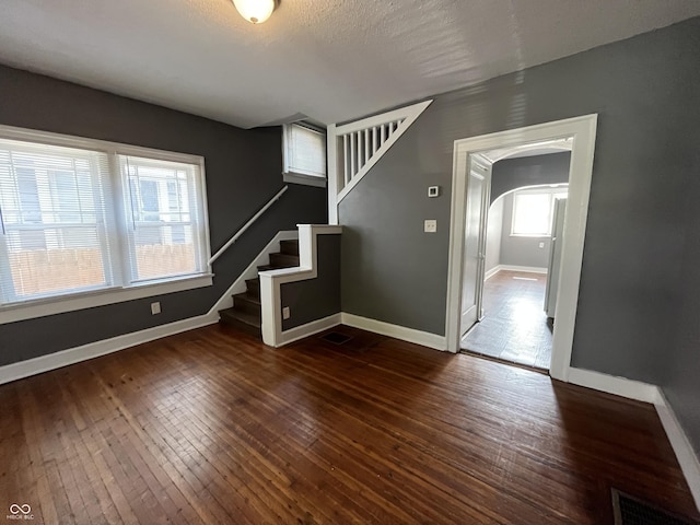 interior space featuring visible vents, baseboards, stairway, dark wood-style floors, and arched walkways