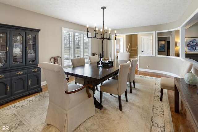 dining area with light wood-type flooring, a textured ceiling, and a chandelier