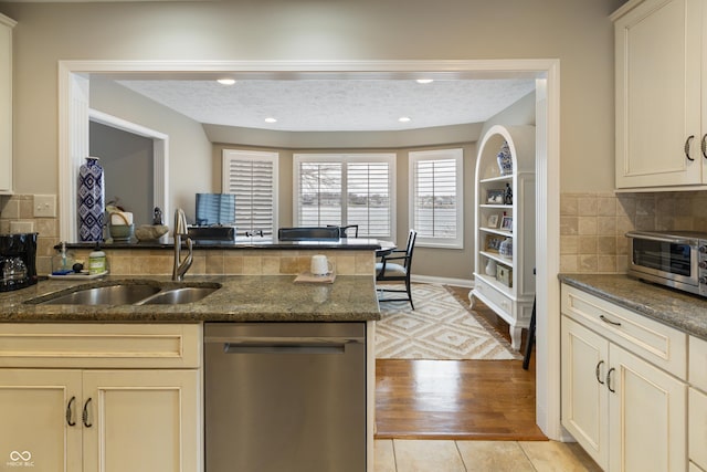 kitchen featuring a toaster, dark stone counters, a peninsula, stainless steel dishwasher, and a sink