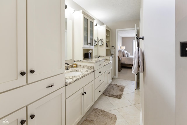 bathroom featuring a sink, a textured ceiling, connected bathroom, tile patterned flooring, and double vanity