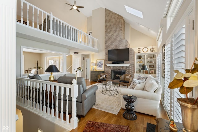 living area featuring a brick fireplace, a skylight, a towering ceiling, wood finished floors, and a ceiling fan