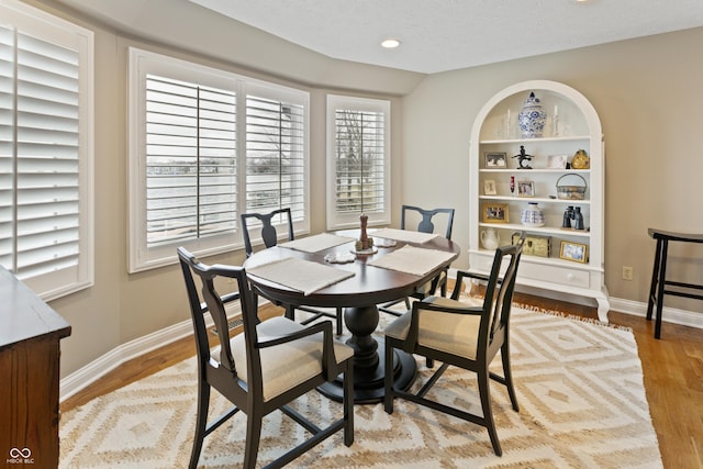 dining space featuring built in features, baseboards, a textured ceiling, and light wood-style flooring