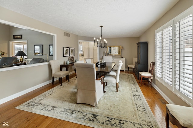 dining room with visible vents, baseboards, an inviting chandelier, wood finished floors, and a textured ceiling