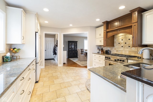 kitchen with recessed lighting, dark stone countertops, high end appliances, and a sink