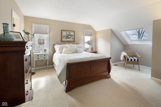 bedroom with vaulted ceiling with skylight, a textured ceiling, light colored carpet, and baseboards