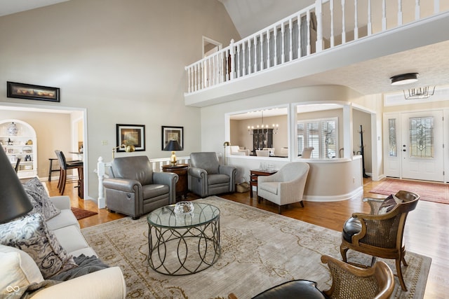 living area with a notable chandelier, wood finished floors, arched walkways, baseboards, and a towering ceiling