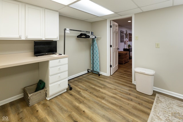 unfurnished office featuring a drop ceiling, baseboards, light wood-type flooring, and built in desk