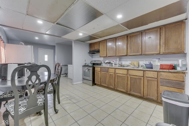 kitchen featuring under cabinet range hood, a drop ceiling, brown cabinetry, and stainless steel range with electric cooktop