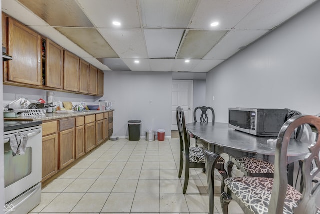 kitchen featuring light tile patterned floors, stainless steel microwave, brown cabinets, and electric range