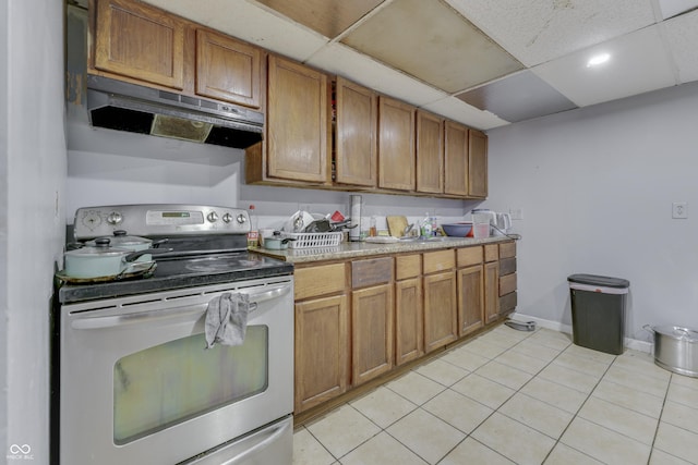 kitchen with light tile patterned floors, light countertops, electric stove, a paneled ceiling, and under cabinet range hood