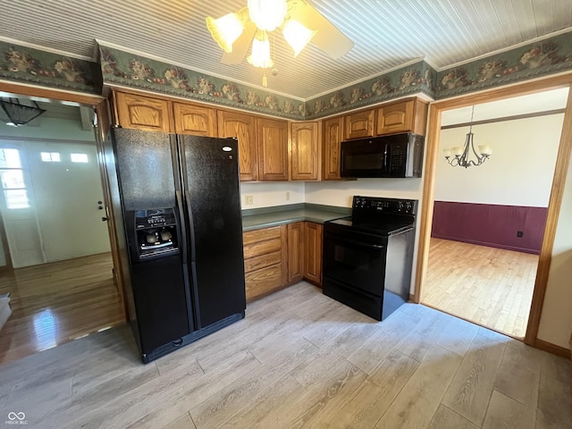 kitchen featuring light wood finished floors, dark countertops, ceiling fan with notable chandelier, brown cabinets, and black appliances