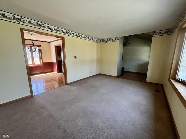 empty room with a notable chandelier, baseboards, and carpet floors