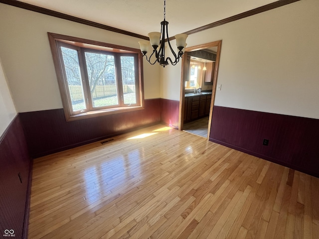 unfurnished dining area featuring light wood-type flooring, a wainscoted wall, visible vents, a sink, and an inviting chandelier