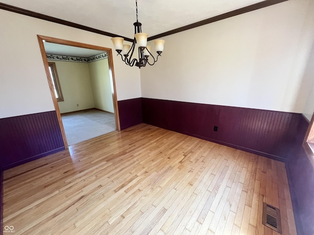 unfurnished room featuring visible vents, crown molding, a wainscoted wall, light wood-type flooring, and a notable chandelier