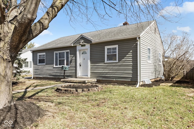 bungalow-style home with a chimney, a front lawn, and a shingled roof