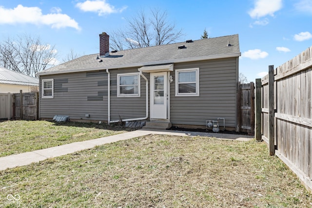 back of house with roof with shingles, a fenced backyard, a chimney, entry steps, and a lawn