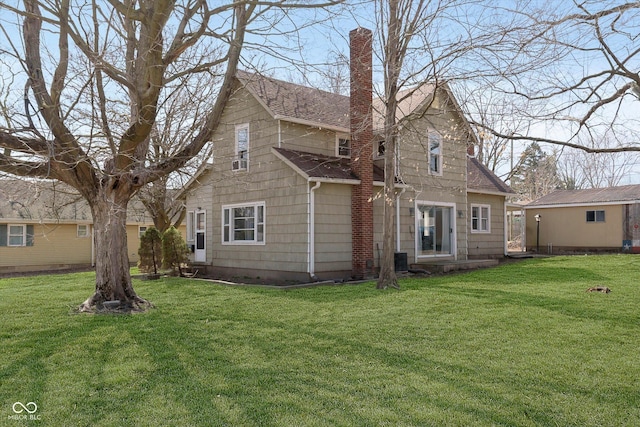 rear view of house featuring a chimney, a shingled roof, and a yard