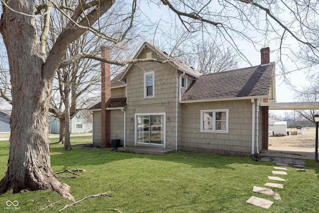 back of house with a yard, central air condition unit, a chimney, and a shingled roof