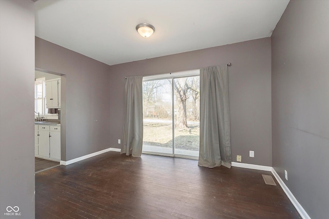 empty room with a sink, baseboards, and dark wood-style flooring