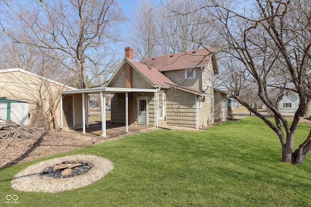 rear view of property with a patio, a shingled roof, a chimney, a fire pit, and a lawn