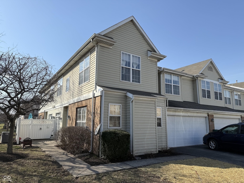 exterior space featuring central air condition unit, an attached garage, fence, and brick siding