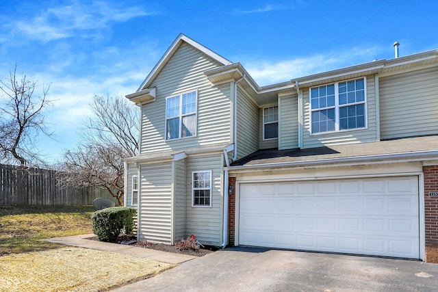 view of front facade with a garage, brick siding, driveway, and fence