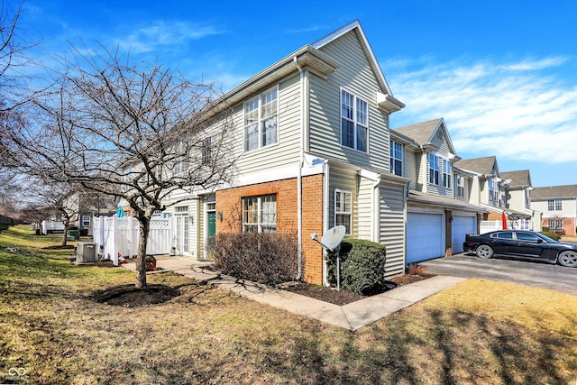 view of side of home featuring brick siding, fence, central AC, a garage, and driveway