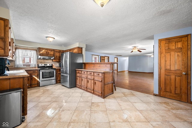 kitchen with a peninsula, brown cabinetry, stainless steel appliances, a ceiling fan, and a sink