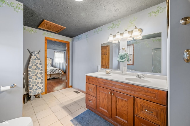 ensuite bathroom featuring a textured ceiling, tile patterned floors, double vanity, and a sink