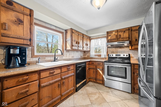 kitchen with brown cabinetry, a sink, light countertops, under cabinet range hood, and appliances with stainless steel finishes