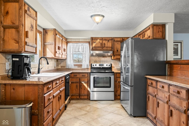 kitchen featuring under cabinet range hood, decorative backsplash, brown cabinetry, stainless steel appliances, and a sink