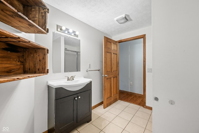 full bath featuring a shower with shower door, a textured ceiling, tile patterned flooring, baseboards, and vanity