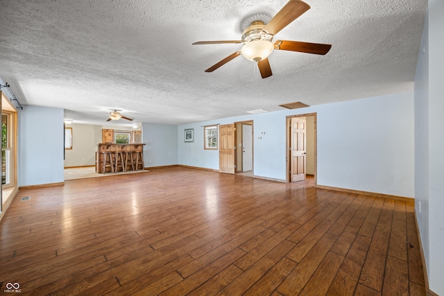 unfurnished living room with a textured ceiling, baseboards, and wood-type flooring