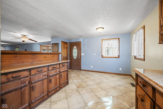 kitchen featuring brown cabinets, a textured ceiling, light countertops, baseboards, and ceiling fan