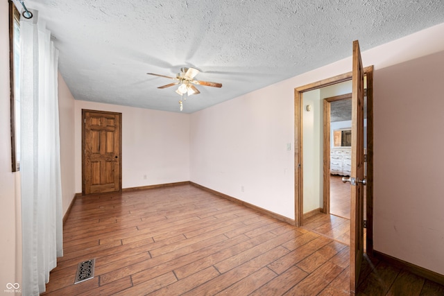 empty room featuring visible vents, baseboards, hardwood / wood-style floors, a textured ceiling, and a ceiling fan