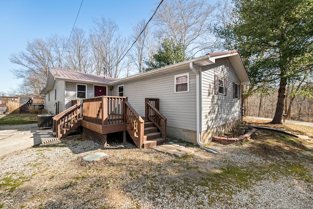 rear view of property with cooling unit, a wooden deck, and metal roof