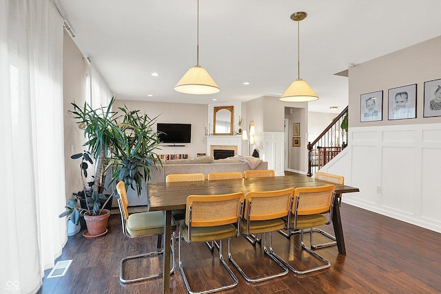 dining room with visible vents, dark wood finished floors, a fireplace, a decorative wall, and stairs