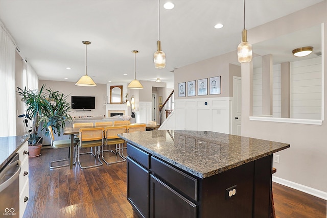 kitchen featuring stainless steel dishwasher, dark wood-style floors, a center island, dark stone counters, and a fireplace