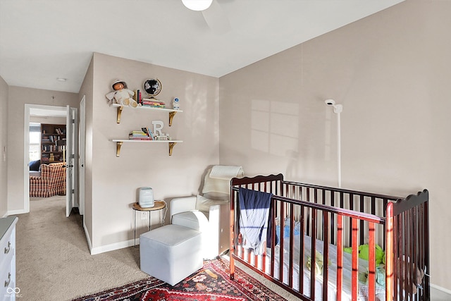 bedroom featuring baseboards, a ceiling fan, a crib, and carpet flooring